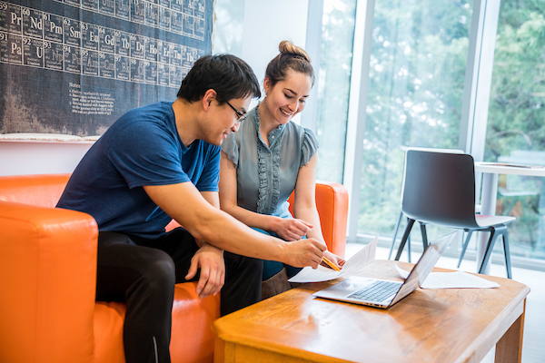 2 students study with notes and a laptop