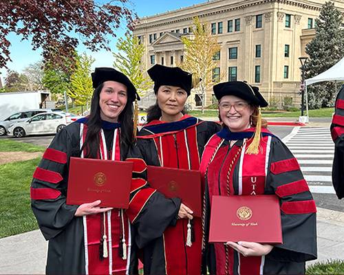 Tessa Washburn, Joy Qiao, and Bridges Eatchel in graduate attire holding diplomas